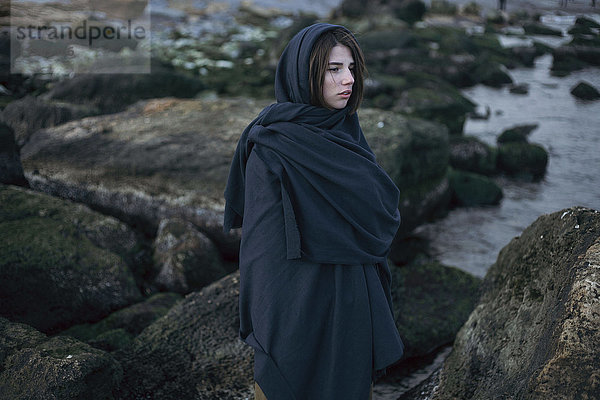 Kaukasische Frau mit Kopftuch auf Felsen am Meer