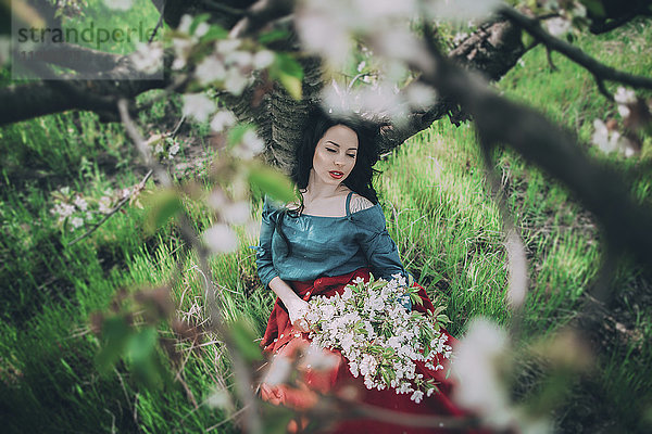 Kaukasische Frau lehnt an einem Baum und hält Blumen