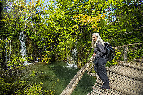 Ältere kaukasische Frau auf Holzbrücke bewundert Wasserfälle