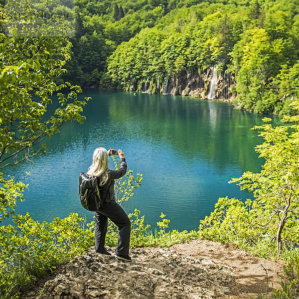 Ältere kaukasische Frau fotografiert Wasserfall mit Handy