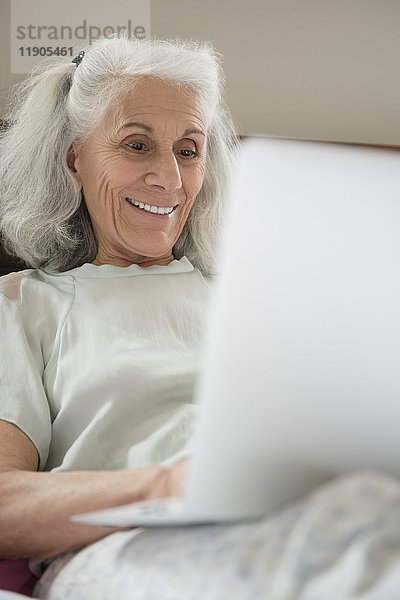 Ältere Frau liegt im Bett und benutzt einen Laptop