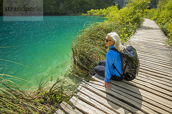 Ältere kaukasische Frau sitzt auf einem Holzsteg in der Nähe von Wasser