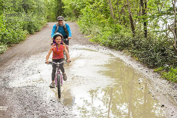 Vater und Tochter fahren mit dem Fahrrad durch eine Pfütze