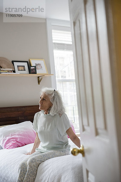 Ältere Frau sitzt auf dem Bett jenseits der Eingangstür