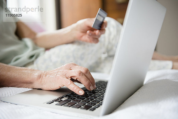 Hände einer älteren Frau beim Online-Shopping mit Kreditkarte und Laptop