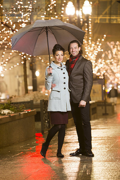 Kaukasisches Paar mit Regenschirm in der Stadt bei Nacht