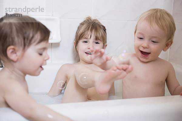 Lächelnde kaukasische Jungen und Mädchen spielen mit Blasen in der Badewanne