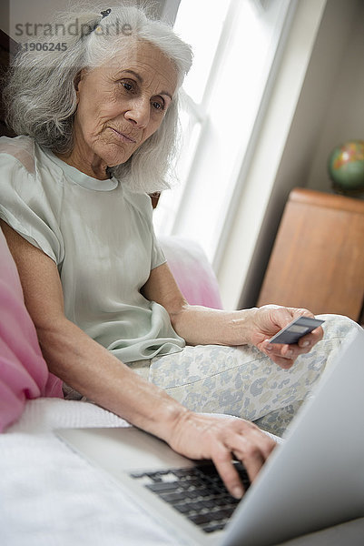 Ältere Frau beim Online-Shopping mit Kreditkarte und Laptop