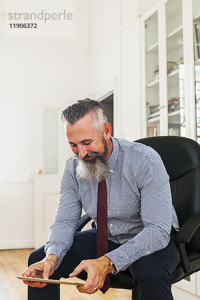 Kaukasischer Geschäftsmann sitzt auf einem Stuhl und benutzt ein digitales Tablet