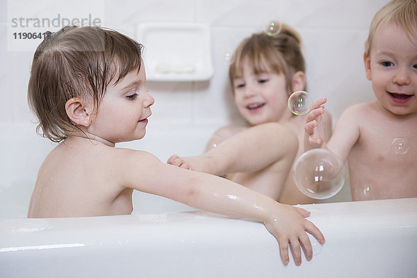 Lächelnde kaukasische Jungen und Mädchen spielen mit Blasen in der Badewanne