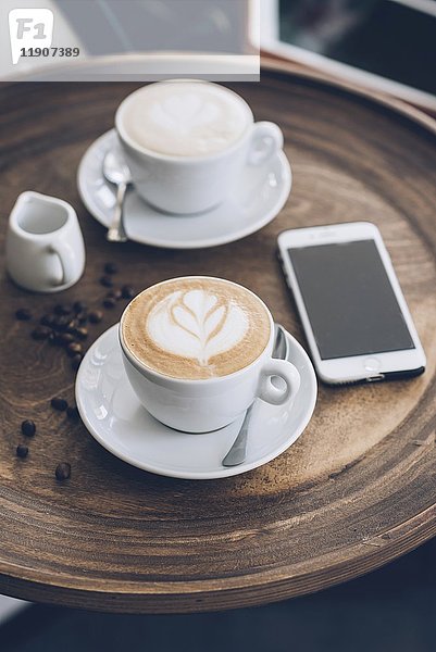 Zwei Tassen Cappuccino neben einem Smartphone auf einem Tisch in einem Café