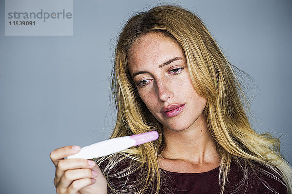 Junge Frau betrachtet Schwangerschaftstest mit enttäuschtem Ausdruck