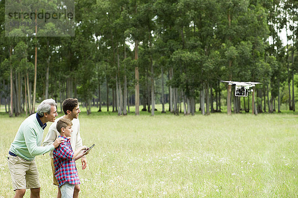 Junge fliegende Fernsteuerungsdrohne im offenen Feld  während Vater und Großvater zusehen.
