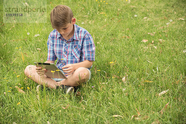 Junge auf Gras sitzend  mit digitalem Tablett