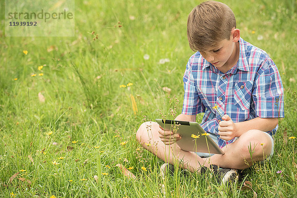 Junge auf Gras sitzend  mit digitalem Tablett