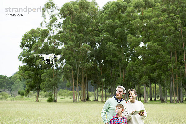 Mann fliegt ferngesteuerte Drohne im offenen Feld  während ältere Männer und Jungen zusehen.