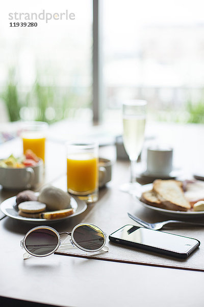 Sonnenbrille und Smartphone auf dem Frühstückstisch im Cafe