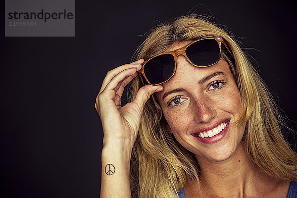 Junge Frau hebt Sonnenbrille und lächelt fröhlich vor der Kamera  Portrait