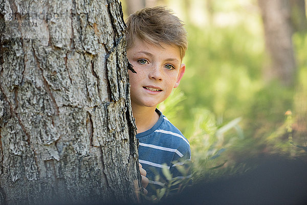 Junge schaut um den Baumstamm  Portrait