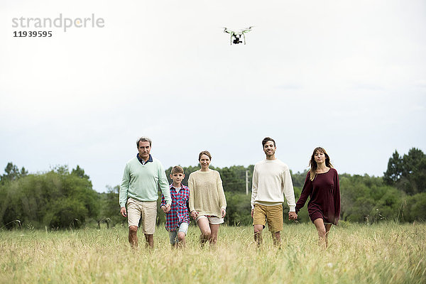 Familie geht zusammen im Feld  während die Drohne über Kopf fliegt.