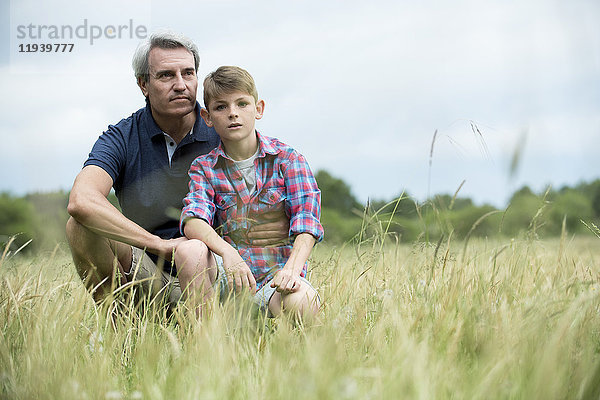Vater und Sohn hocken zusammen im hohen Gras.