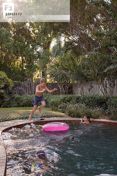 Kinder schwimmen im Gartenpool  ein Junge springt hinein  in der Luft