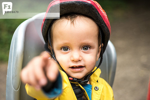 Porträt eines Jungen  der im Kindersitz eines Erwachsenenfahrrads sitzt  zeigt auf