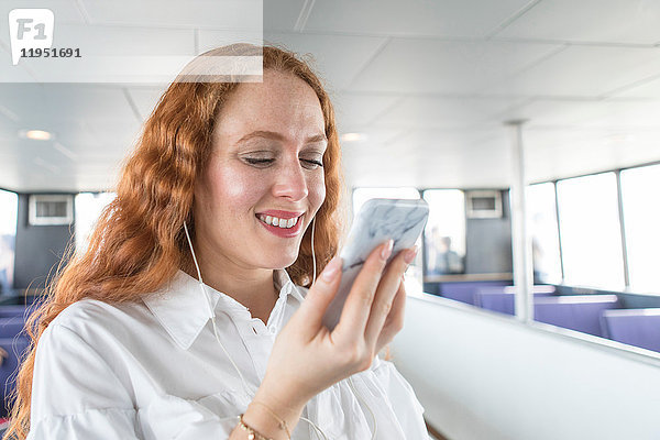 Lächelnde junge Geschäftsfrau betrachtet Smartphone auf Passagierfähre