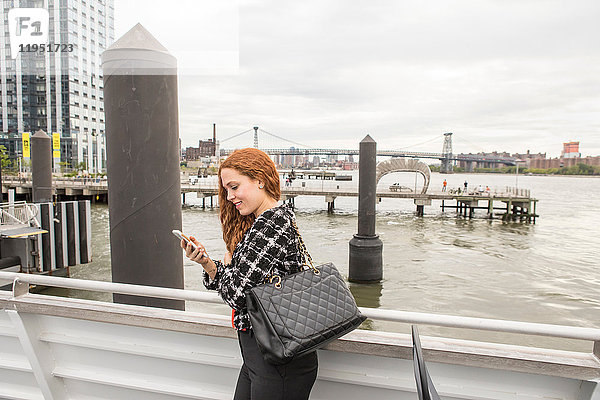 Junge Geschäftsfrau auf dem Fährdeck mit Blick auf Smartphone  New York  USA