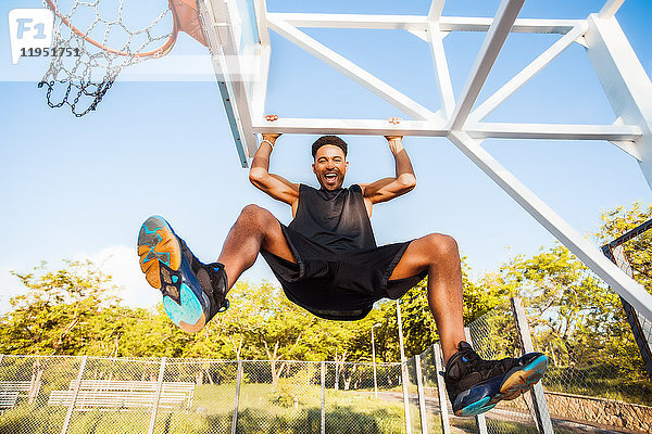 Junger Mann auf dem Basketballplatz  auf Basketballnetzrahmen schwingend  niedriger Blickwinkel