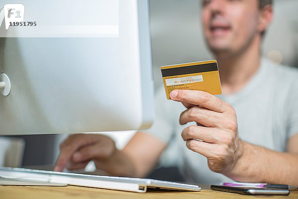 Geschnittene Ansicht eines Mannes  der mit einem Computer eine Kreditkarte hält