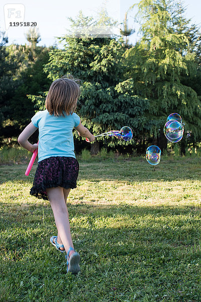 Junges Mädchen spielt mit dem Blasenzauberstab im Garten  Rückansicht