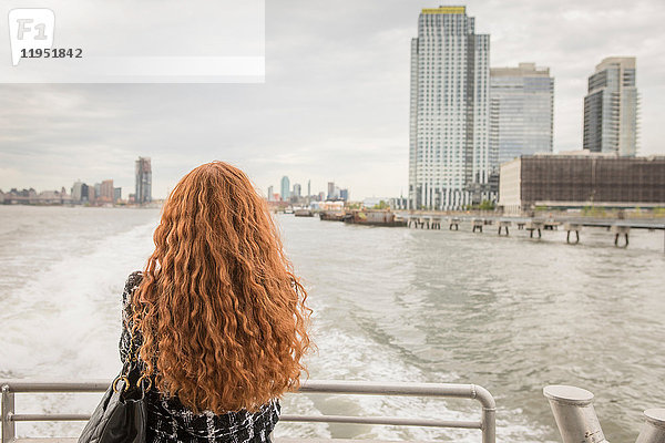 Rückansicht einer langhaarigen rothaarigen Geschäftsfrau auf dem Fährdeck mit Blick auf die Skyline  New York  USA