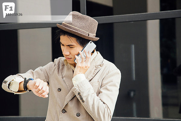 Junger Mann im Freien  benutzt Smartphone  schaut auf Armbanduhr