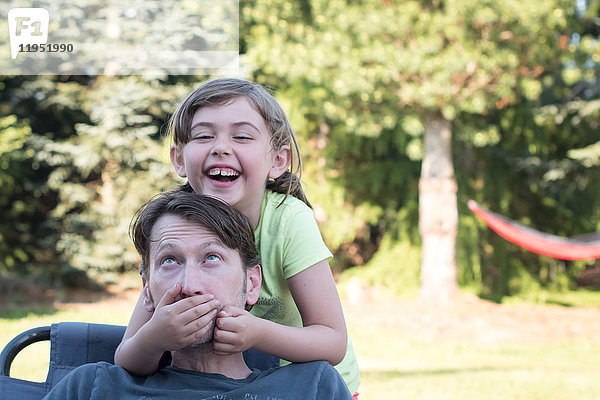 Vater und Tochter treiben sich im Freien herum  junges Mädchen bedeckt den Mund des Vaters  lacht