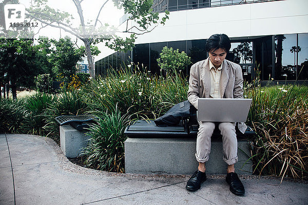 Junger Mann sitzt im Freien und benutzt Laptop