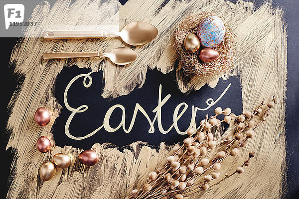 Draufsicht auf gefärbte und goldbemalte Ostereier und -löffel mit handgeschriebenen Ostern