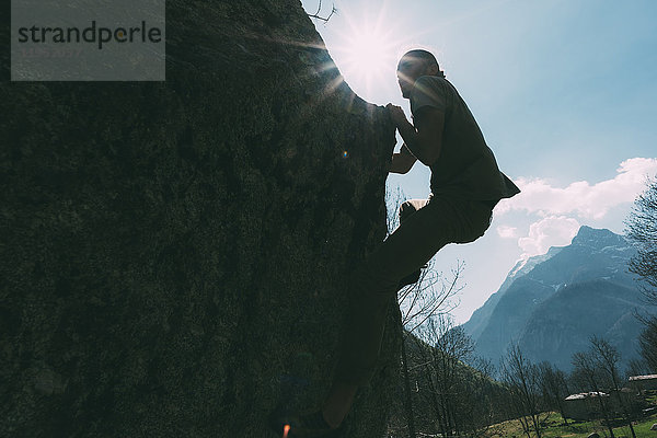 Hinterleuchtete Ansicht eines jungen männlichen Boulderers beim Klettern  Lombardei  Italien