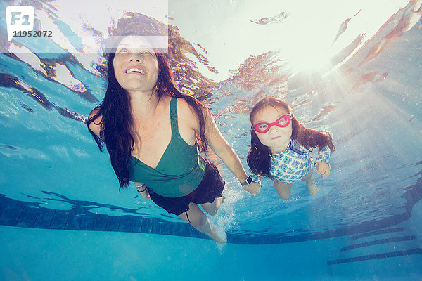 Unterwasseransicht einer reifen Frau  die schwimmend die Hand ihrer Tochter hält