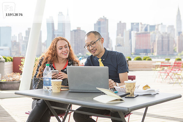 Geschäftsmann und -frau schauen auf einen Laptop im Hafencafé mit der Skyline von New York  USA