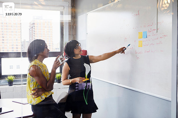Zwei Frauen im Büro  Problem lösen  Whiteboard benutzen  Haftnotizen auf Whiteboard kleben
