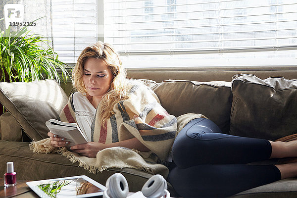 Frau liest Buch auf dem Sofa