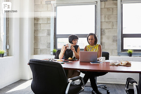 Zwei Frauen sitzen am Tisch im Sitzungssaal und benutzen einen Laptop