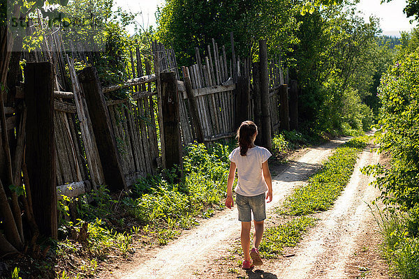 Rückansicht eines einsamen Teenager-Mädchens  das auf einem ländlichen Feldweg spazieren geht