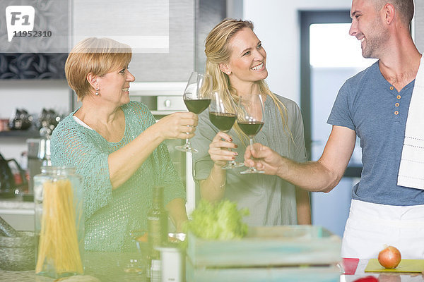 Drei Freunde in der Küche  die Weingläser halten und einen Toast ausbringen