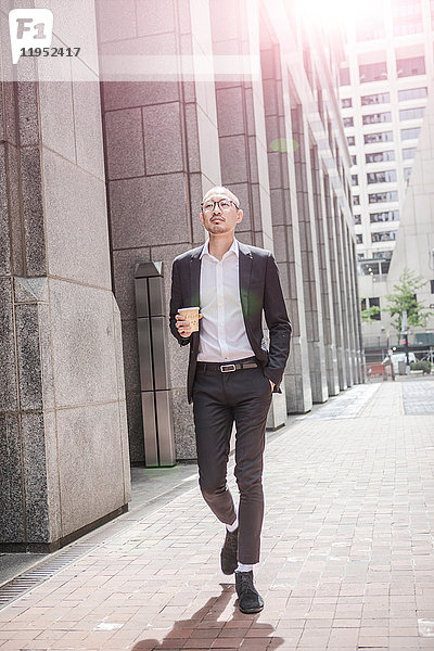 Cooler Geschäftsmann mit Kaffee zum Mitnehmen schlendert über den Bürgersteig  New York  USA