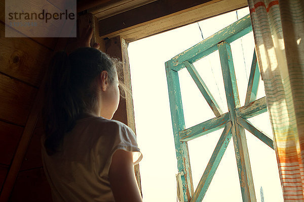 Teenager-Mädchen schaut aus dem sonnenbeschienenen Schlafzimmerfenster