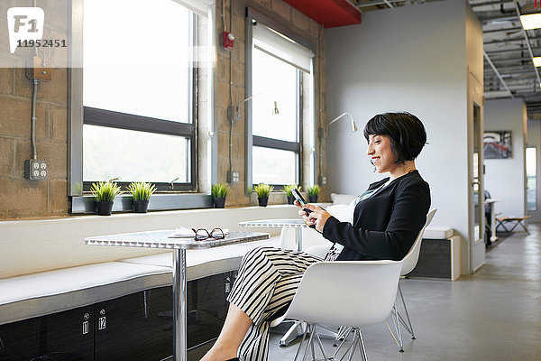 Geschäftsfrau sitzt am Tisch in einer Büroumgebung und schaut auf ein Smartphone