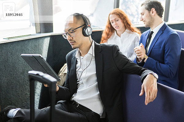 Geschäftsmann  der auf der Passagierfähre Kopfhörer hört und auf ein digitales Tablet schaut