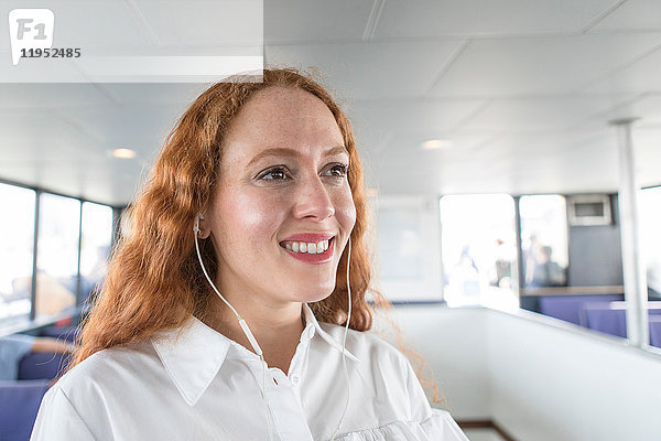 Lächelnde junge Geschäftsfrau hört Kopfhörermusik auf der Passagierfähre
